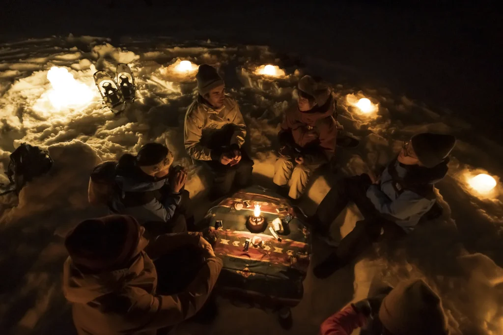 Snowshoers gathered around lanterns in the snow during a night walk in a Nagano forest