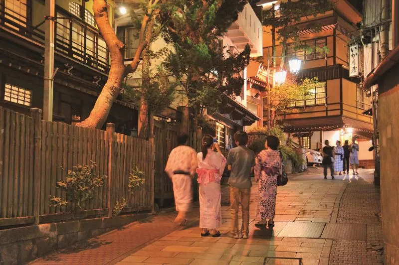 Guests in yukata walking a lantern-lit lane in a snowbound hot spring town