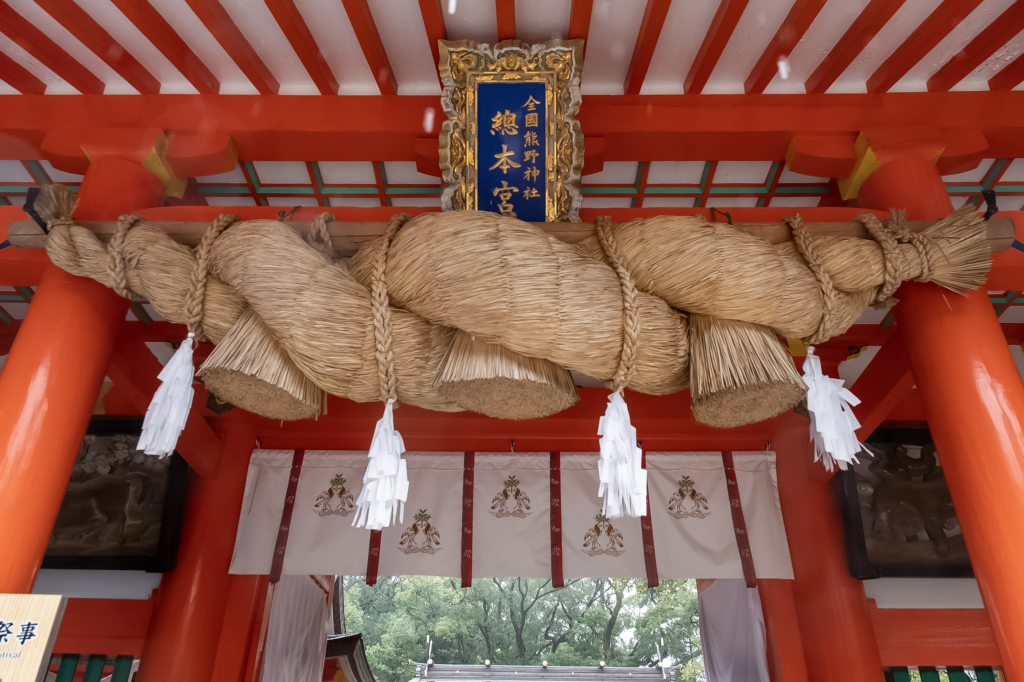 A thick shimenawa rope hanging beneath the vermilion eaves of Kumano Hayatama Taisha