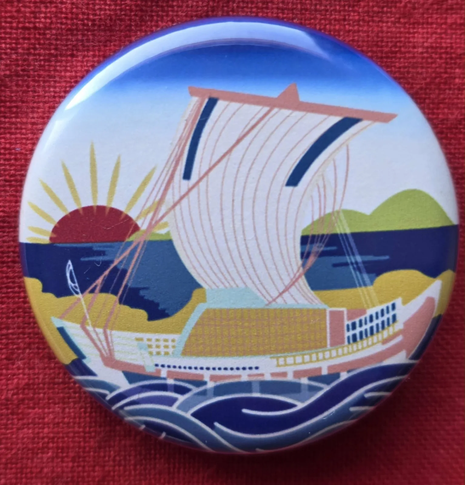 A stylized drawing of a kitamaebune domestic trading ship on a souvenir button