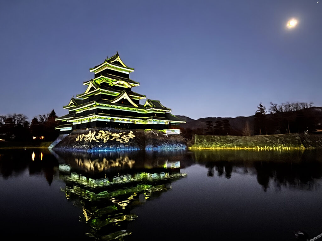 Matsumoto Castle lit up at night and reflected in the still water of its moat