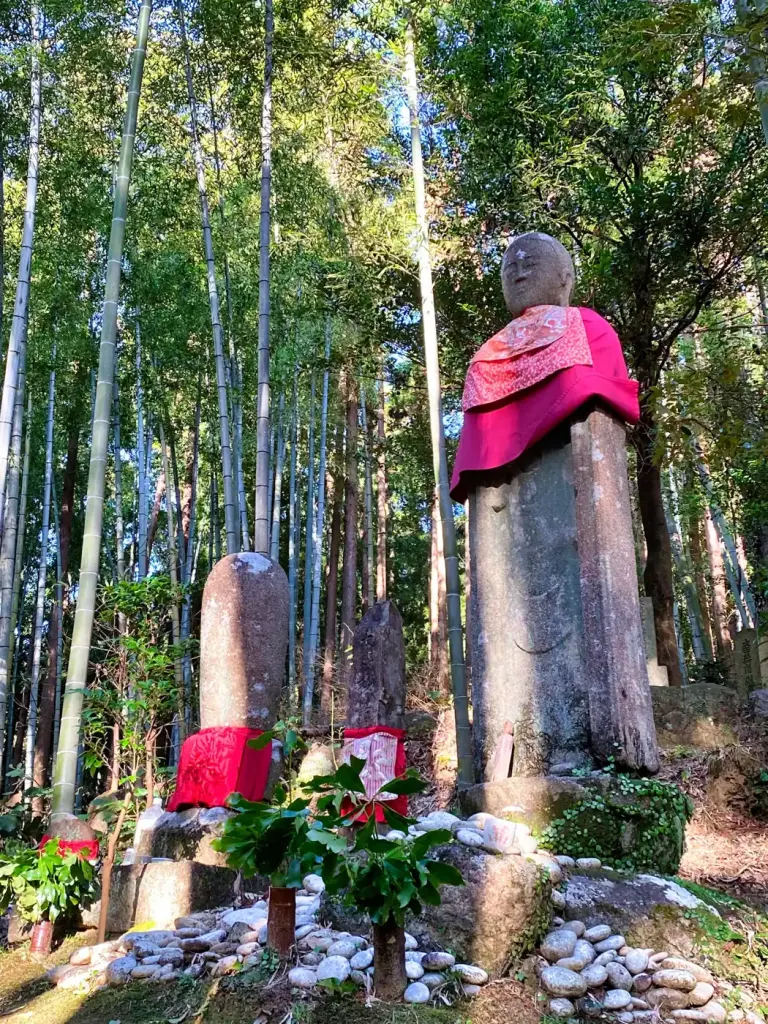 A stone Jizo statue wearing a red bib in a bamboo grove on the Kumano Kodo Iseji route