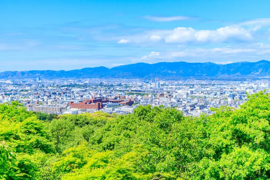 The Kyoto cityscape seen over green treetops from the surrounding hills