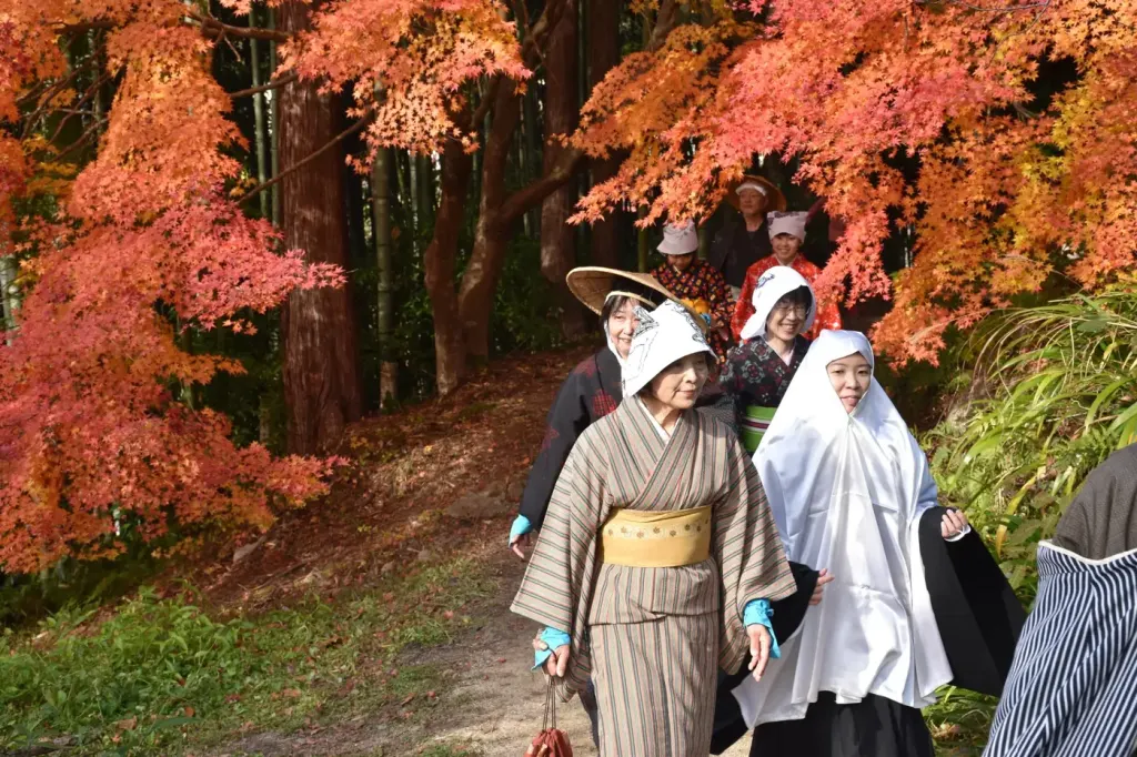 Walkers in Edo-period costume passing beneath bright autumn maples on the Nakasendo